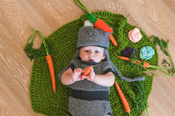 Baby girl in bunny hat lying on green blanket and carrot in his hands