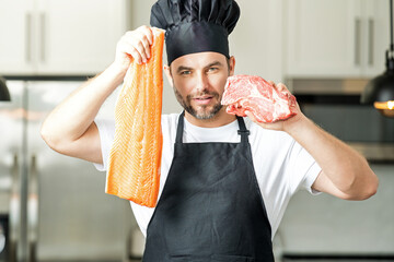Portrait in kitchen of chef preparing healthy food. Man cooking fish and meat, salmon and beef....