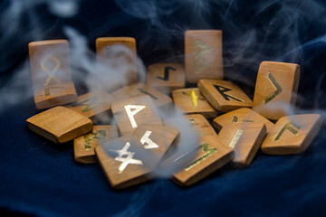 A lot of gray and thick smoke covers the wooden runes, which lie on a black background.	

