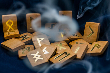 A lot of gray and thick smoke flies around the wooden runes, which lie very close on a black...