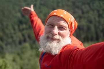a white elderly man takes a selfie on the top of a mountain, against the background of the sky and...