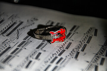 A ring in the form of a guitar lies on the page of a book with notes.	
