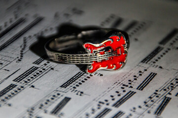 A ring in the form of a red guitar lies on the page of a book with notes close-up	
