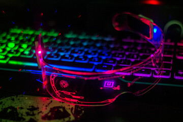 Glowing red futuristic glasses with transparent glass lie on a multi-colored keyboard close-up	
