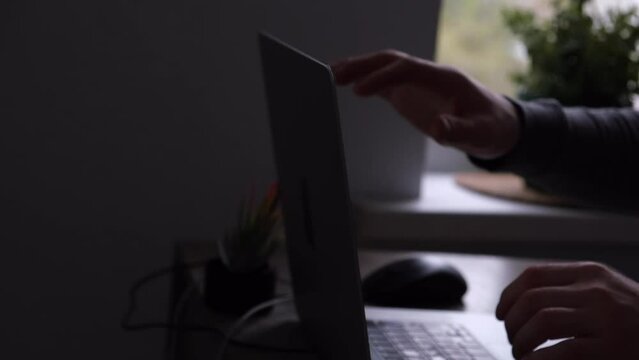 An unrecognizable man in gray closes his laptop after work. The concept of a job done or completion of a working day or project, remote work, freelancing.