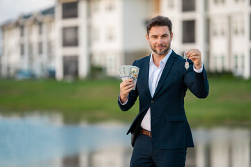 Handsome real estate agent holding money dollars and house keys. Man real estate agent in business suit presenting the house for sale. New apartment after buying real estate.
