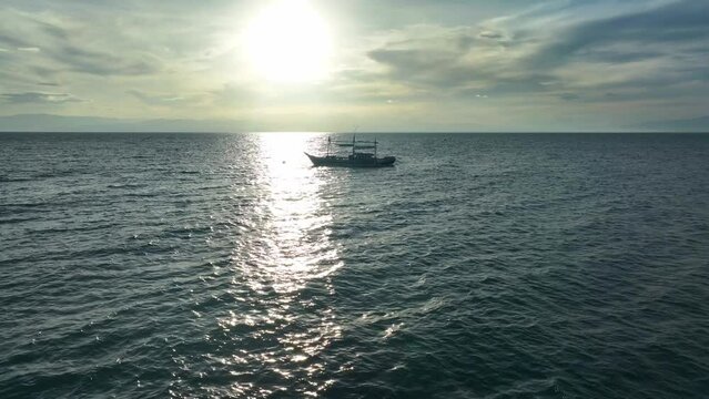 Drone approaching shot of beautiful seascape and boat with sun reflects on water surface. Silhouette of traditional fishing boats named bangka in Philippines.