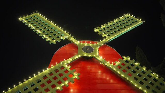 Blades of a festive Christmas windmill decorated with garlands rotate against the background of the night sky