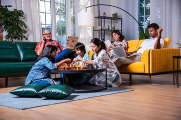 Indian asian multigenerational family playing chess in living room at home