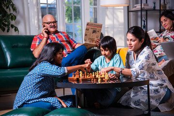 Indian asian multigenerational family playing chess in living room at home