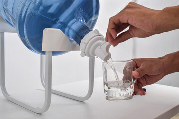Man's hand pours water into a glass cup from a large gallon. Pouring fresh clear water from a large...