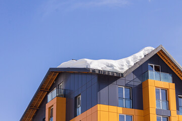 Dangerous snow falls from the roofs of the buildings. Winter with heavy snowfall. Snow falls above sidewalks with people. Uncleaned snow