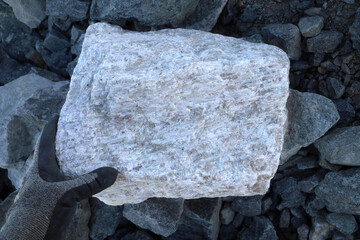 Hand, protective glove, large pegmatite spodumene ore rock amongst waste (barren in lithium)....