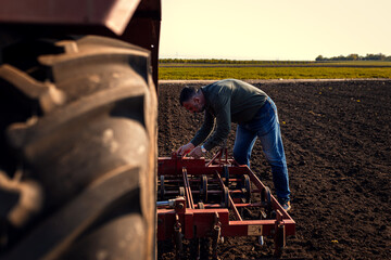 Portrait of farmer standing in field preparing harrow to cultivate the land with a tractor.