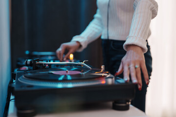 Close-up of a female DJ's hands adjusting vinyl on turntable, setting the party vibe.