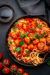 Italian spaghetti pasta in marinara sauce with meatballs, black table background, top view