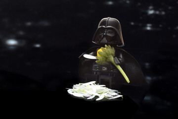Naklejka premium Lego minifigure of Darth Vader or Star Wars male army is sitting with daisy flower isolated on black. Editorial illustrative image to Mother's Day.