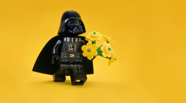 Lego minifigure of Darth Vader or Star Wars male army is walking with flowers in hand isolated on yellow. Editorial illustrative image to Mother's Day.