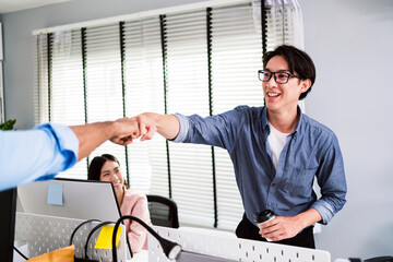 Cheerful Asian businessman partners making fist bump with a smile as a symbol of teamwork. Positive...