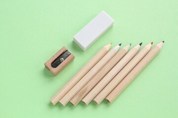 Colored pencils, wooden manual sharpener and eraser on green background. Back to school concept. Set of writing tools for education, creativity, drawing, hobby, art. Eco-friendly stationery