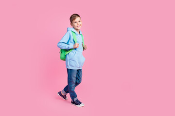 Full body profile photo of little positive boy carry backpack walk empty space isolated on pink...