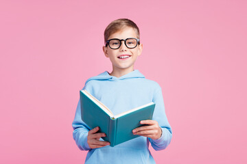 Portrait of cute clever positive schoolkid toothy smile hold opened book isolated on pink color...