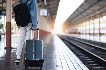 A young man holding a suitcase waits for a train at the train station for traveling.