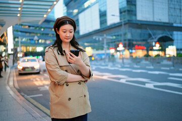 Fototapeta premium Young Woman Using Smartphone in Bustling City Evening