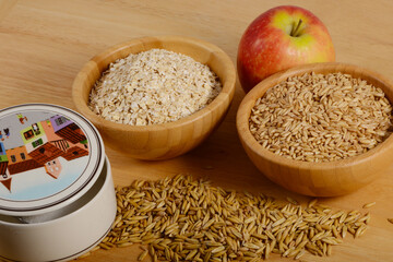 Geschälter Hafer und Haferflocken in kleinen Holzschälchen, mit einem Häufchen Spelzenhafer, Apfel und  Zuckerdose  umrahmt,  Zutaten für ein Müsli, Sachaufnahme