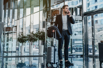 Male business traveler standing and talking on mobile phone in airport hallway. Business talk....