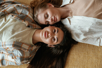 Lying down on the floor. Two happy young female best friends are indoors