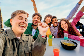 Group of diverse friends selfie - laughing and enjoying drinks at a beach gathering, showing joy and togetherness in a casual outdoor setting.