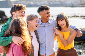 A lively group of diverse friends laugh together during a casual outing by the sea, showcasing genuine happiness and strong bonds in a natural setting.