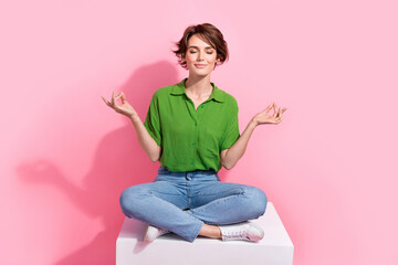 Full size photo of peaceful focused woman dressed green shirt jeans sit on cube in meditation pose...