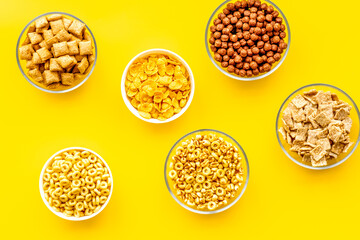 Various corn cereals in bowls on yellow background top view pattern