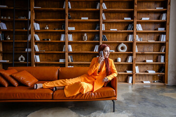 Red-haired girl talking on a mobile phone in an orange business suit while sitting in the library