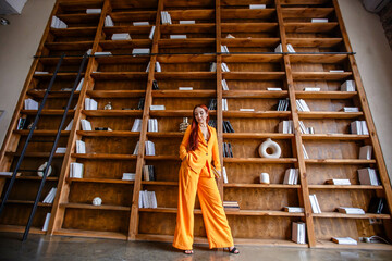 Red-haired girl in an orange business suit posing in the library