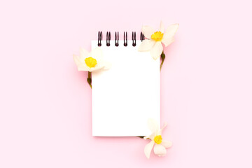 Blank notepad mockup with white narcissus flowers on a pink background. Spring creative concept.