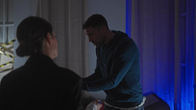 A policewoman interrogates a suspicious man in a dimly lit indoor scene, suggesting a serious investigation.