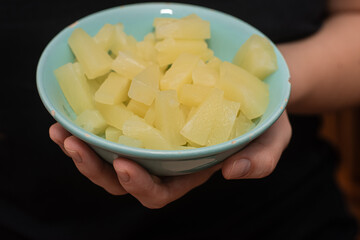 Serving Bowl of Diced Pineapple. Close-up view of a person's hands holding a bowl of freshly diced pineapple pieces, ready to eat