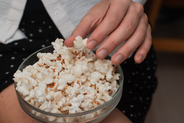 Woman Holding Bowl of Fresh Popcorn. Close-up of a woman's hands holding a transparent bowl filled with freshly popped popcorn, on a natural woven mat.