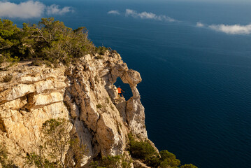 Sportive young man climbing to the Eye of Es Vedra viewpoint rock in Ibiza, Sant Josep de Sa Talaia. Balearic Islands, Spain