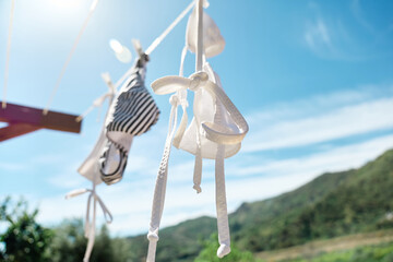 White woman  bikini swimsuit hanging air drying on line in summer sunny windy day. Swimwear, pareo and straw hat flutter on the wind. Summer concept of vacation, relax, holiday.