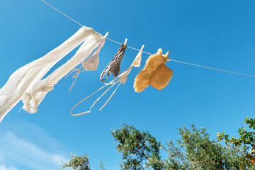 White woman  bikini swimsuit hanging air drying on line in summer sunny windy day. Swimwear, pareo and straw hat flutter on the wind. Summer concept of vacation, relax, holiday.