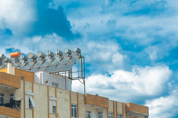 Fototapeta premium Urban Rooftop with Water Tanks and Satellite Dishes. City building rooftop filled with water tanks and satellite dishes against a cloudy sky backdrop.