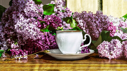 A bouquet of purple lilac flowers and a white vintage cup of coffee with a spoon on a wooden...