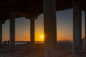 Sunset Seen Through Supports of Huntington Beach Pier, with Random Unrecognizable people Scattered on Sand, California, USA, vertical