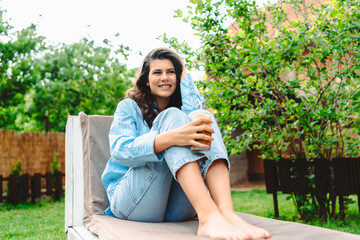 One young caucasian woman is relaxing on easy bed while drinking cold coffee in her backyard	