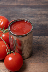 Tomato sacue  in opened tin can, fresh tomatoes around, on old wooden table, portrait format