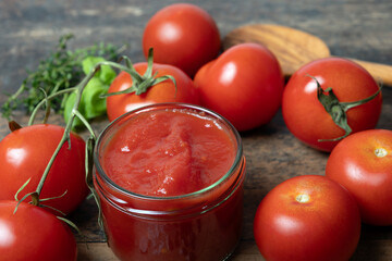 Traditional, homemade tomato sauce in glass, with ingredients basil, thyme, salt, pepper, stands on a wooden table